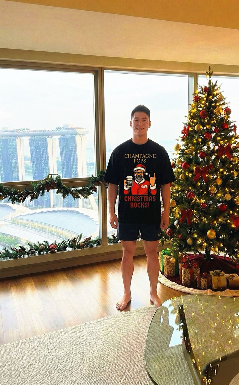 Person wearing a Christmas Rock and Roll shirt in front of a decorated Christmas tree indoors.
