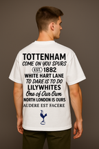 Man wearing a white t-shirt with Spurs Perfect10 and a logo on the back, standing against a brown background

